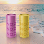 Load image into Gallery viewer, Purple and Yellow colored Nözscreen bottle sitting at beach shore. 
